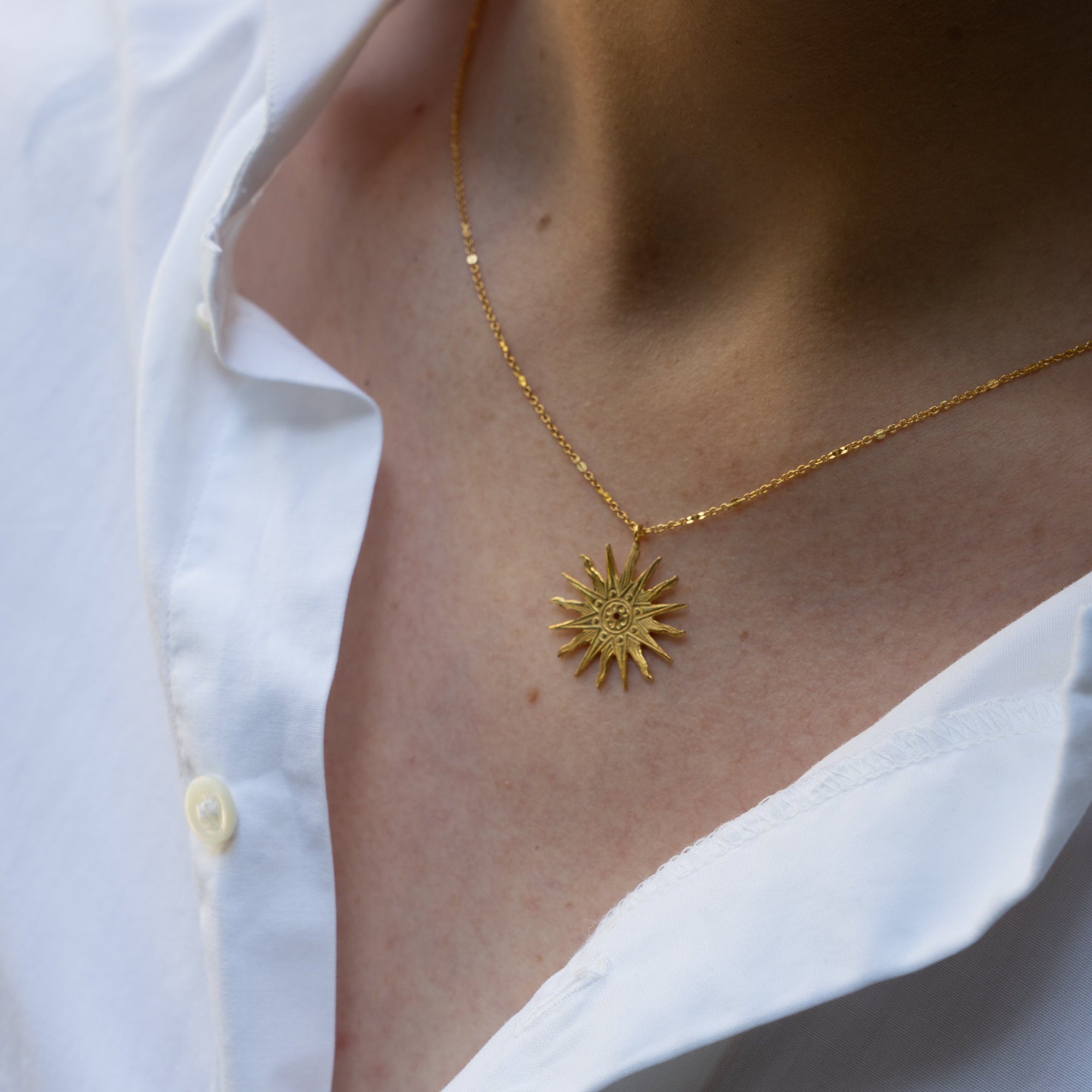 photo close up du collier doré heure royale porté par une modèle à la chemise blanche