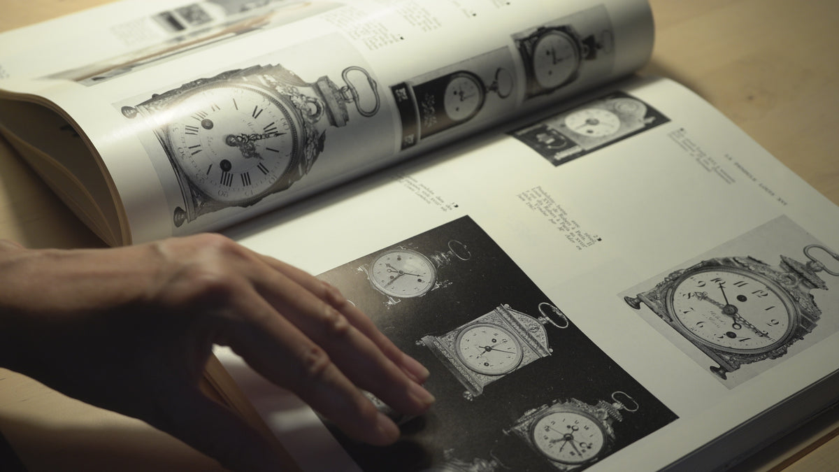 Marie-Louise parcourt son encyclopédie de l'horlogerie et montre les modèles qui ont inspirés sa collection Royale